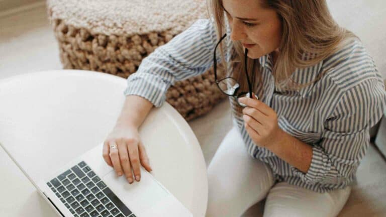 A girl working on her laptop and holding her glasses