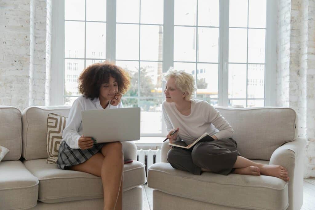 two women sitting on a sofa with a laptop