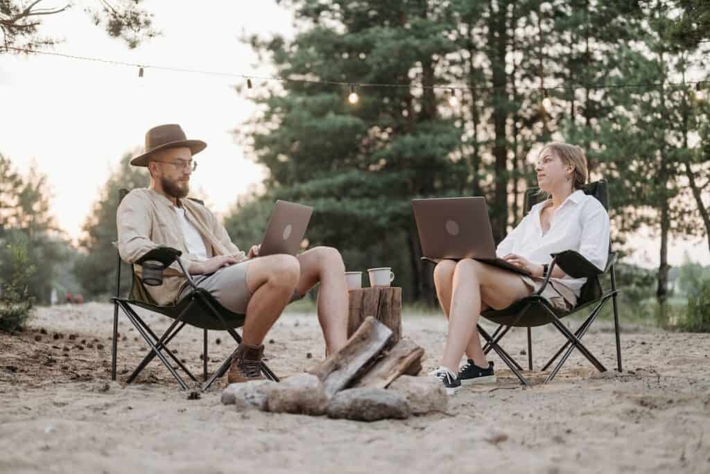 man and woman working on their laptop in a campsite