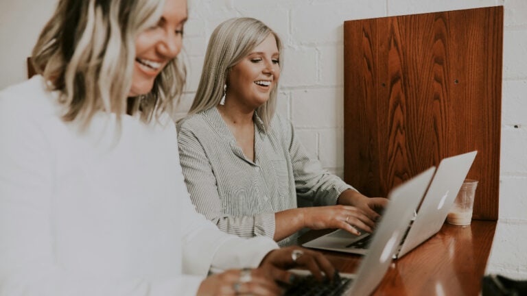 Two girls behind laptop smiling