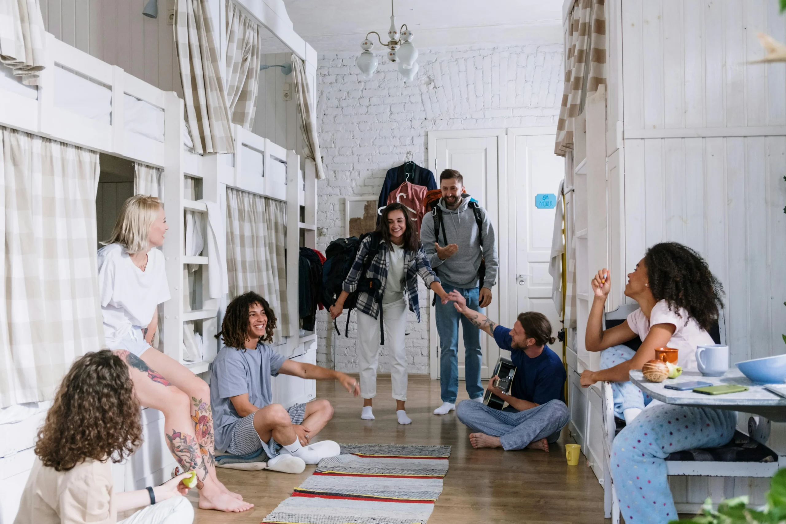 A diverse group of young adults socializing in a cozy, modern coliving dormitory with bunk beds and a relaxed atmosphere.