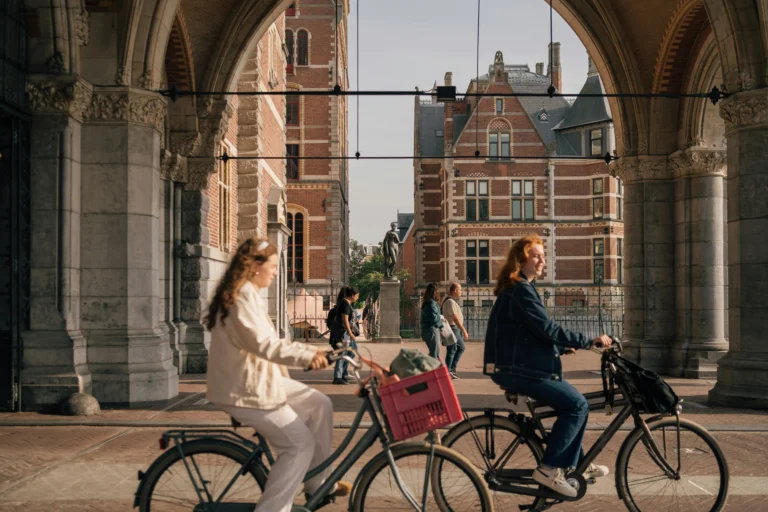 People cycling under an archway in Amsterdam, with historic buildings in the background