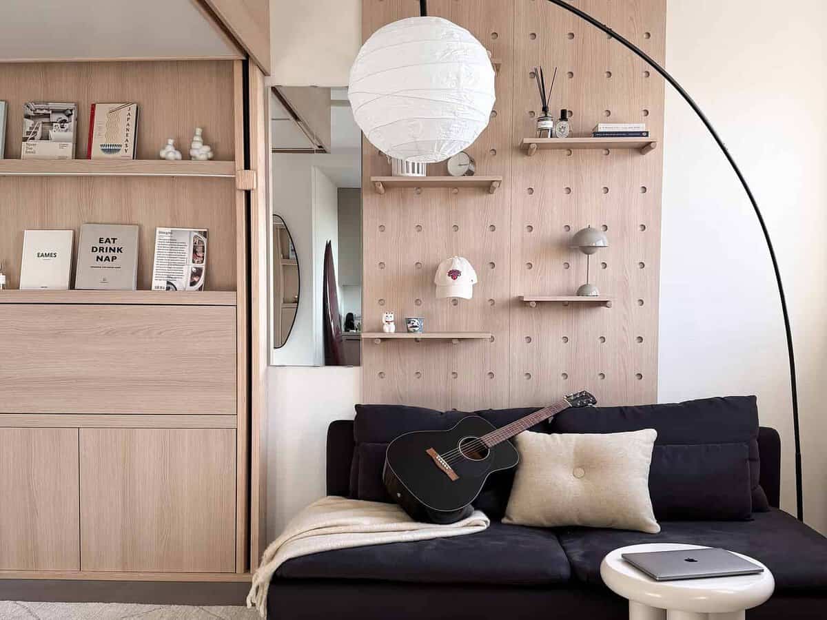 Stylish small living space with pegboard wall, bookshelves, a black couch, and personal items like a guitar and decor.