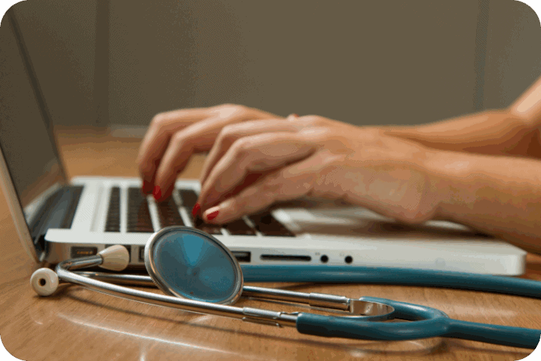 Woman typing on a laptop with a stethoscope in the foreground