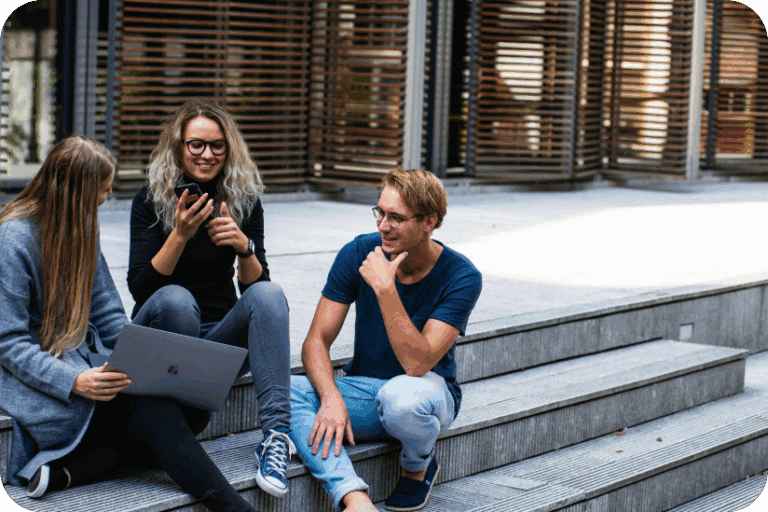 Three students sitting on campus steps with a laptop