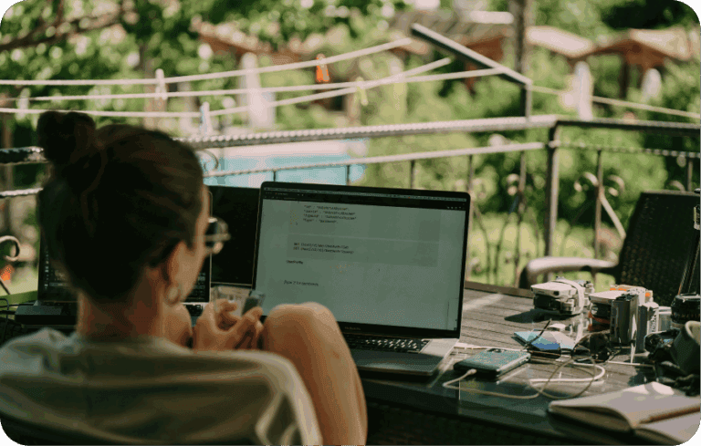 Woman working on laptop outdoors at a patio with tech and greenery