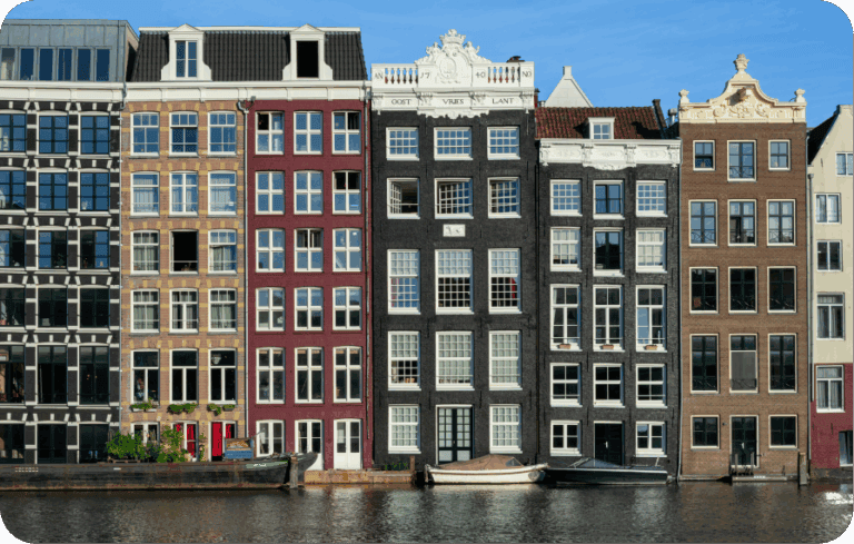 Row of colorful historic canal houses with boats docked along the water in central Amsterdam