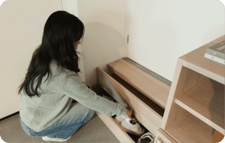 Woman placing shoes into a wooden genkan-style shoe drawer