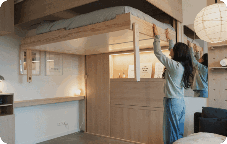 Woman folding up a wall-mounted wooden bed in a small apartment